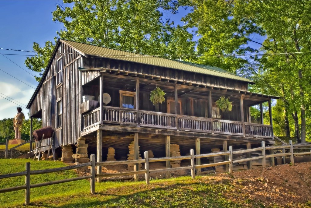 A historic log cabin situated on a grassy hillside with a split-rail fence