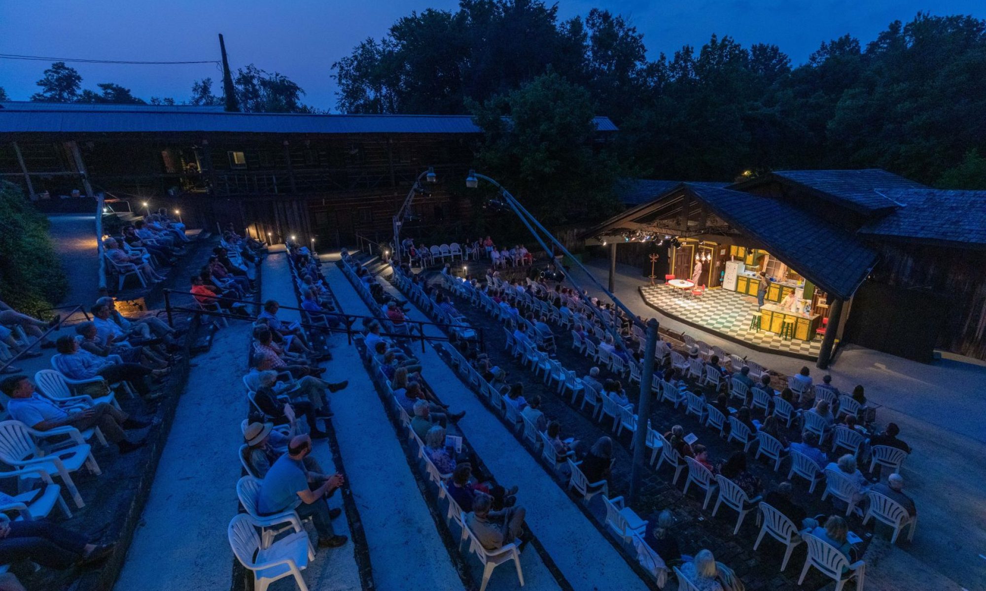 Folks seated in chairs enjoy an evening concert at an outdoor amphitheater.