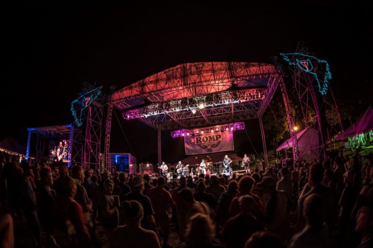 A crowd enjoys a stage at night, with neon owl signs.